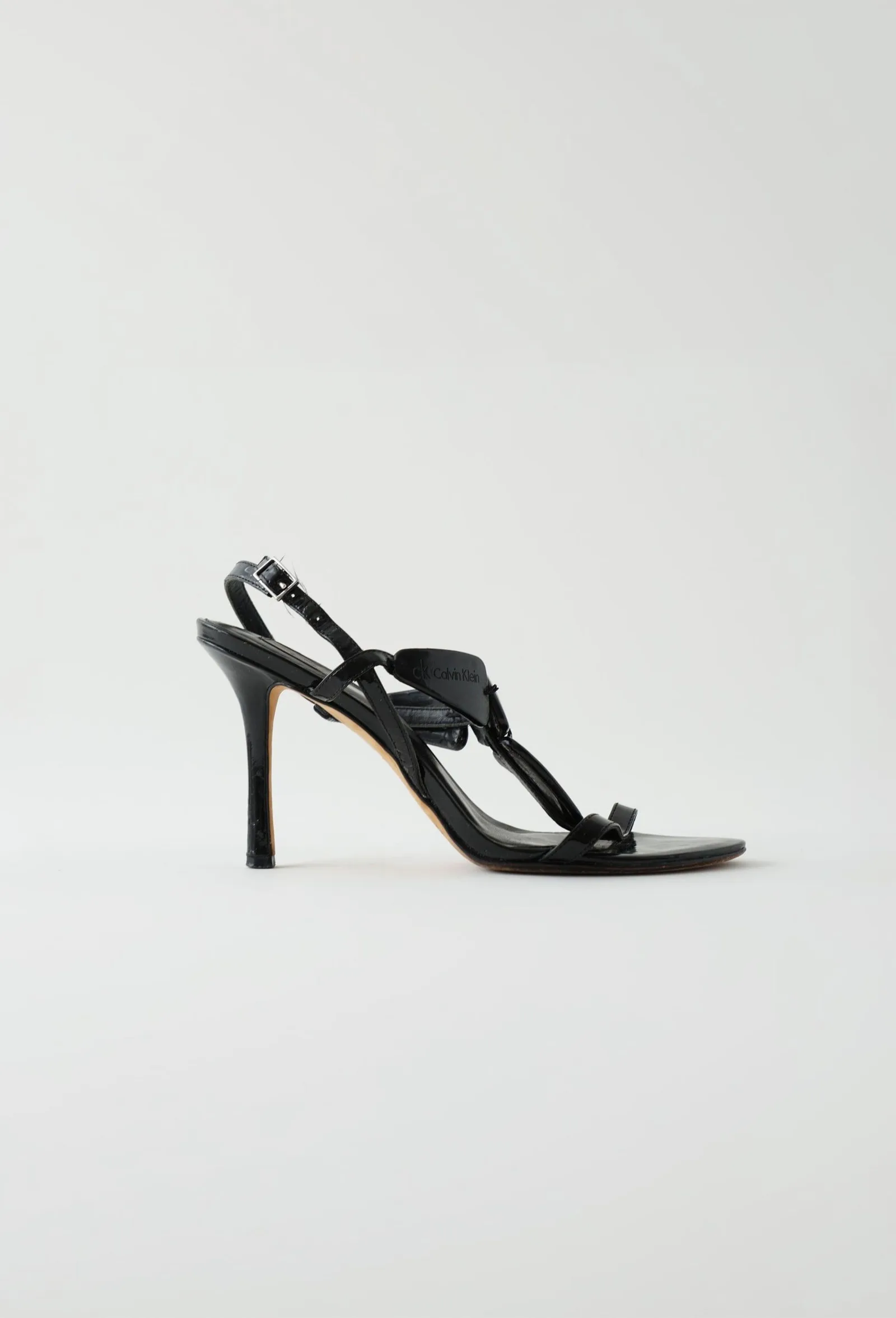 Black patent-leather Calvin Klein stiletto sandal with crossover straps, side profile.