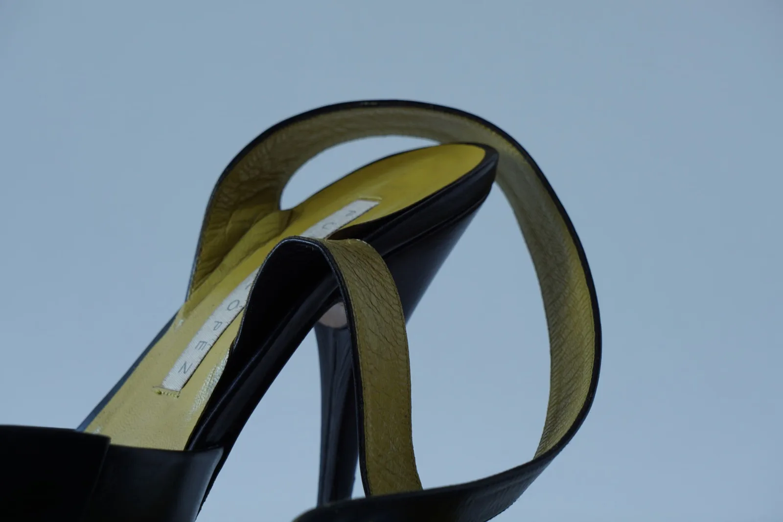 Close-up of the olive-gold woven ankle strap and black heel counter.