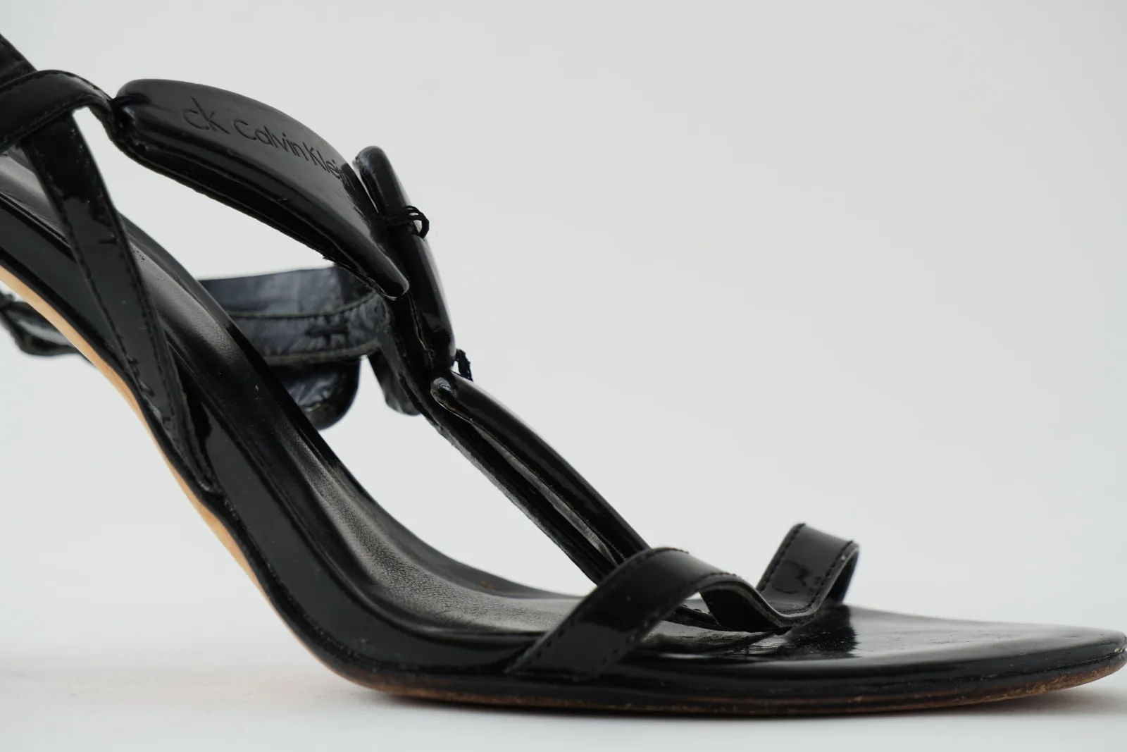 Close-up of encre toe straps, glossy patent finish and curved insole.
