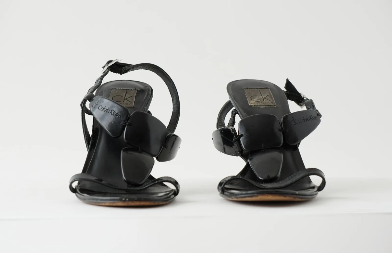Front view of the pair of black patent encre sandals and their crossover straps.