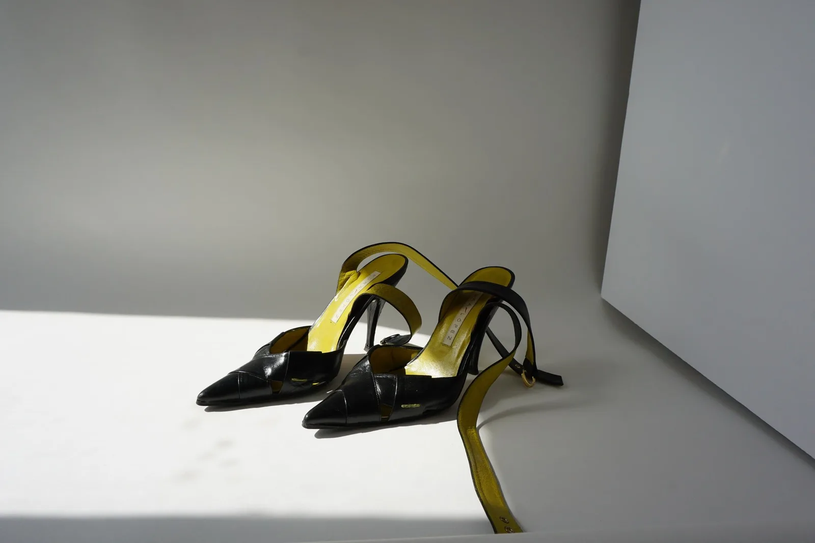 Pair of black onyx of sable heels with trailing ankle straps on a studio floor.