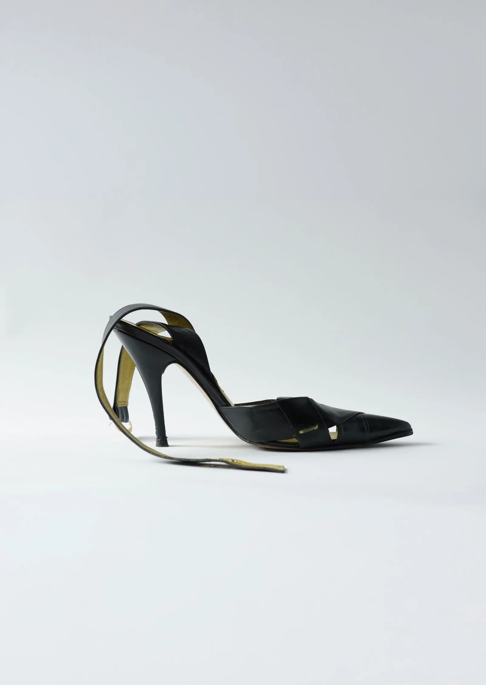 Black pointed-toe stiletto with olive-gold woven ankle straps, side profile.