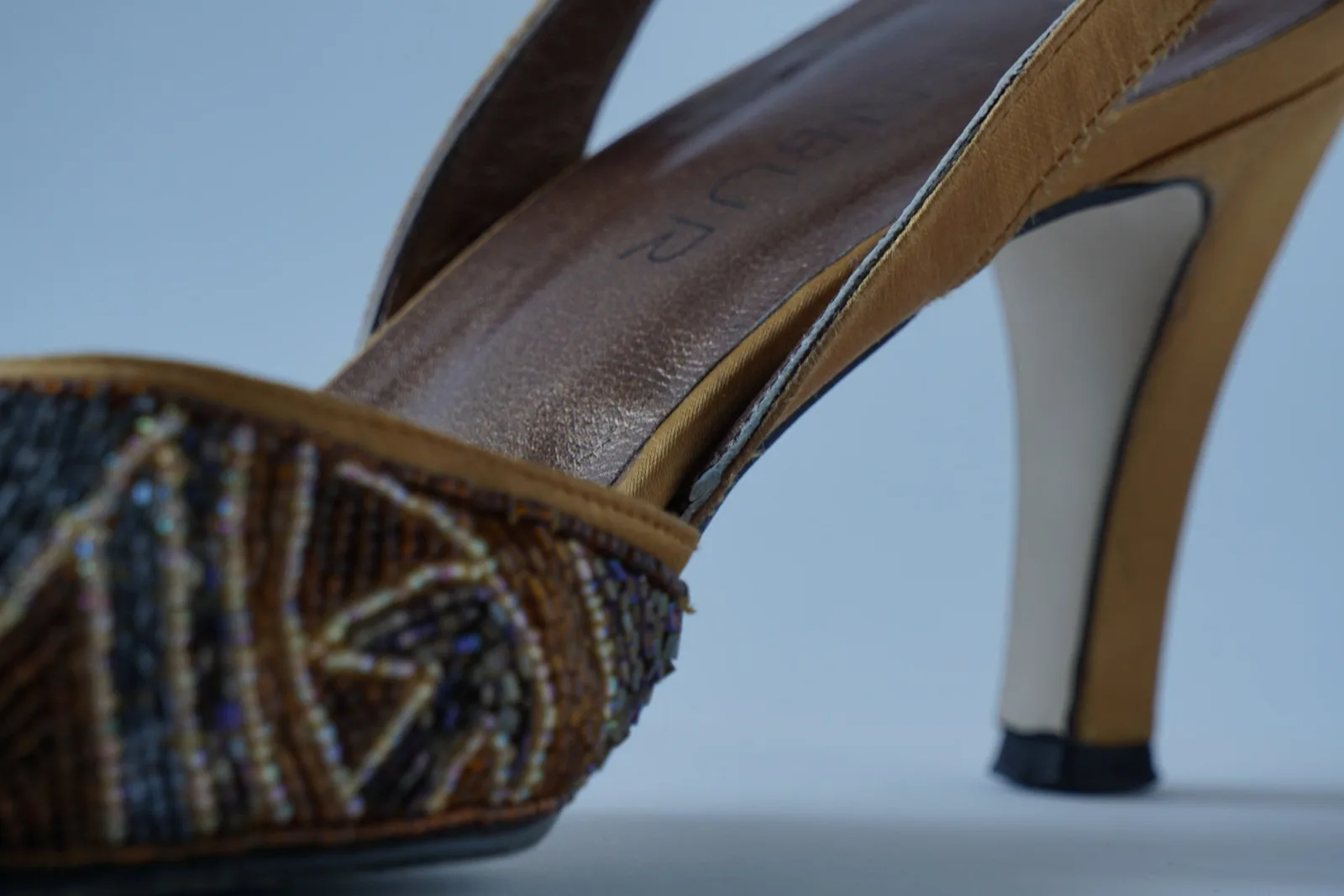 Close-up of bijou beadwork, leather slingback and golden heel.